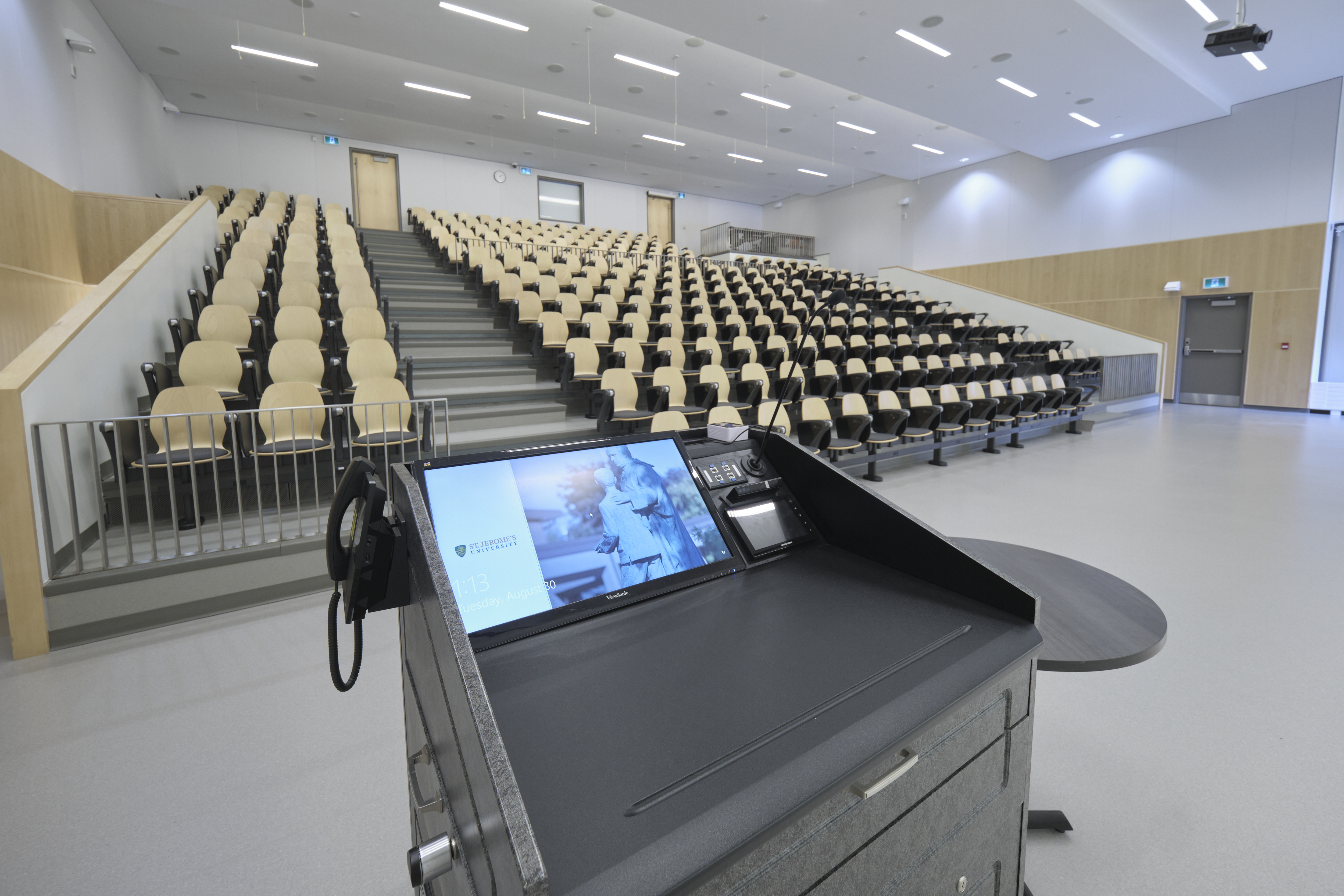 A large theatre with fixed tier seating and a multimedia lectern at the front.