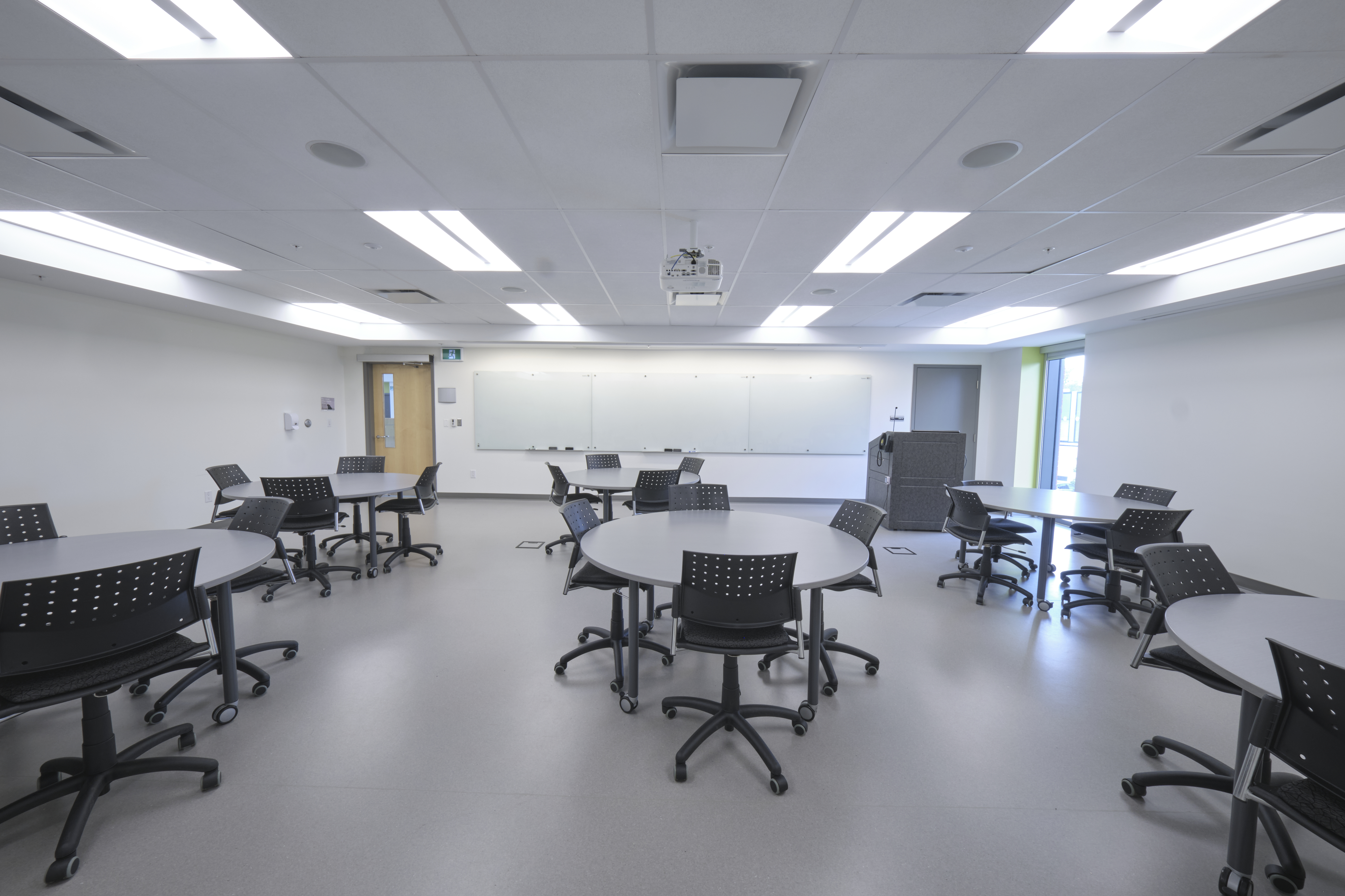 A room with round tables and a lectern and whiteboard at the front.