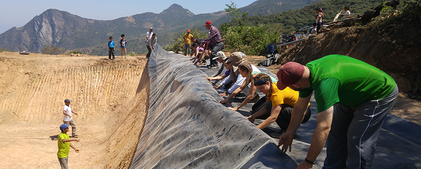 A line of people push a tarp across a field in Peru