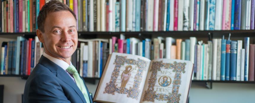 Image of a men holding book in hand and book shelf in background