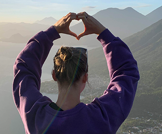 Image of a person sitting on a mountain showing a heart with their hands