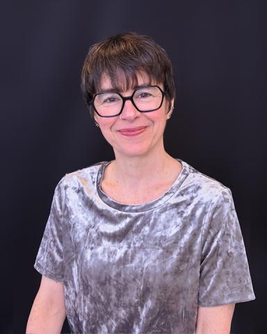 Tristanne poses wearing a silver velvet shirt and smiles in front of a black background